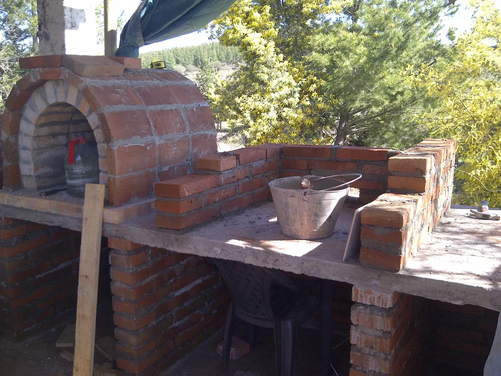 Un horno de barro y ladrillo junto a un mesón, al aire libre
