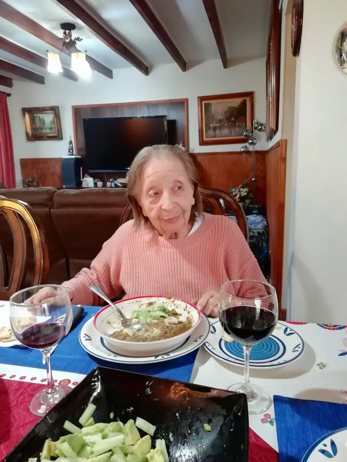 Una mujer mayor sonríe en la mesa, frente a un plato de comida